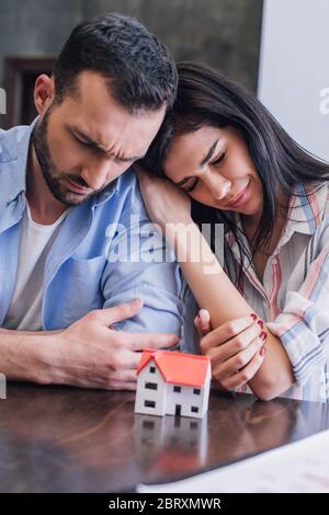 Donna piangendo e appoggiandosi a un uomo teso vicino al modello di casa a tavola Foto Stock