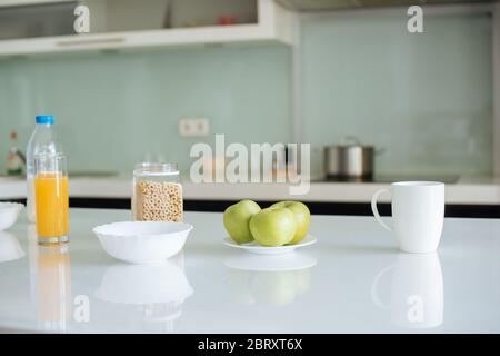 fiocchi di mais, mele, latte, succo d'arancia e tazza di caffè per la colazione in cucina Foto Stock
