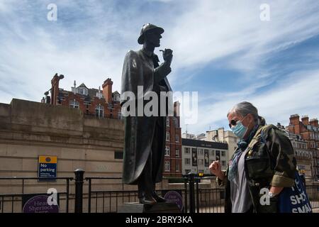 Una donna che indossa una maschera facciale cammina davanti alla statua di Sherlock Holmes fuori dalla stazione della metropolitana di Baker Street a Londra il giorno di Sherlock Holmes, dopo l'introduzione di misure per portare il paese fuori dalla serratura. Foto Stock