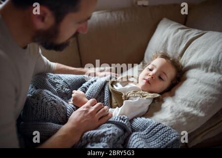 Padre che controlla la figlia piccola malata che si trova in letto all'interno della casa. Foto Stock