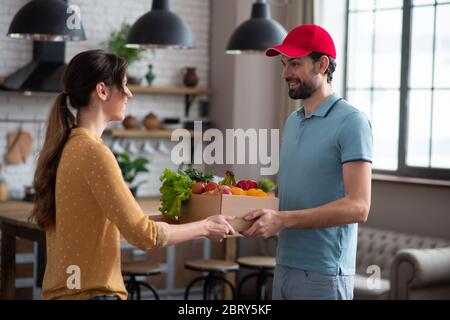 Giovane cliente dai capelli scuri che riceve generi alimentari dal corriere Foto Stock