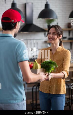 Cliente femminile dai capelli scuri che riceve generi alimentari dal corriere e che si sente bene Foto Stock