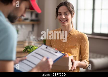 Giovane Courier maschio in un cappello rosso guardando la lettera di vettura e scrivendo qualcosa Foto Stock