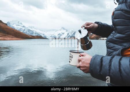 Mani umane di un viaggiatore che versa il caffè in una tazza da una macchina per caffè espresso. Avventura, viaggio, trekking e campeggio concetto a Bachalpsee la Foto Stock