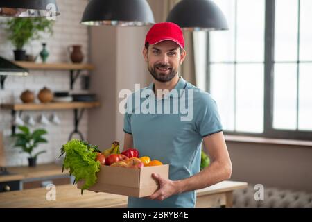 Uomo in un cappello rosso che tiene la scatola con gli alimentari sul tavolo Foto Stock