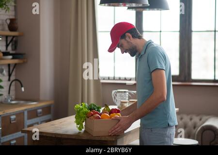 Uomo in un cappello rosso mettendo la scatola con gli alimentari sul tavolo Foto Stock