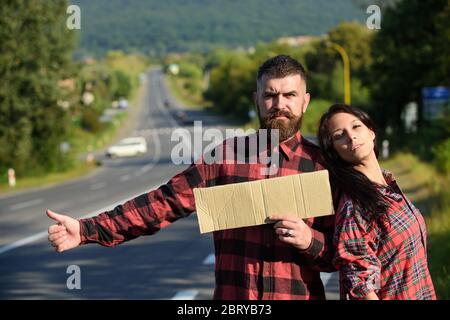 Avventura e hitchtrekking concetto. Coppia con volti pensivi viaggia con auto stop. Coppia innamorata viaggiando su hitchtrekking, spazio copia. Uomo e donna cercano di fermare l'auto con cartoncino, pollici su. Foto Stock