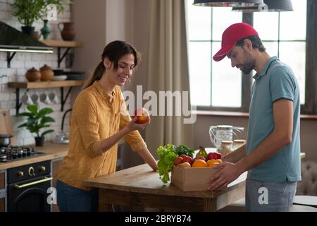 Donna che riceve la consegna di cibo a casa da un corriere e che tiene una mela Foto Stock