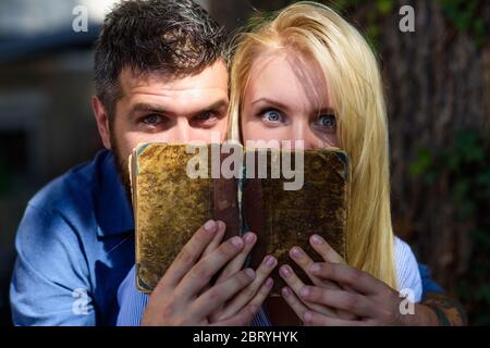 Coppia in amore leggere libro antico, sfondo scuro. Volti stupiti di coppia nascosti da vecchio libro disordinato. Uomo e donna hanno trovato informazioni scioccanti nel vecchio notebook. Concetto di libro stupefacente. Foto Stock