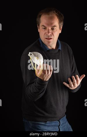 Un uomo confuso che tiene una maschera medica, DPI Foto Stock