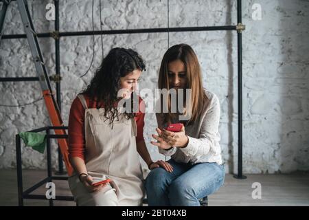 Due donne mid adulte che guardano lo smartphone nel loro nuovo negozio Foto Stock