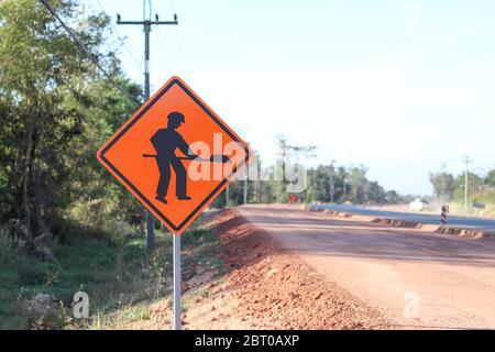 Il segno arancione mostra un simbolo con l'immagine di una persona che tiene una pala sul cartello montato sul lato della strada di costruzione. Avviso di accesso Foto Stock
