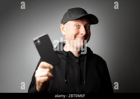 Uomo in abiti neri felice con il messaggio sul telefono o il telefono stesso Foto Stock