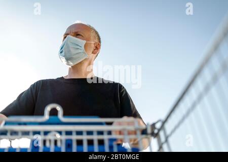 Uomo che indossa maschera protettiva per il viso spingendo carrello pronto per lo shopping nel supermercato Foto Stock