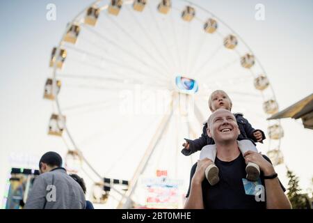 Felice padre con il suo piccolo figlio piggybacked in un parco di divertimenti Foto Stock