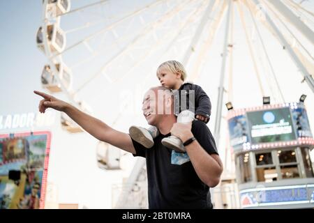 Felice padre con il suo piccolo figlio piggybacked in un parco di divertimenti Foto Stock