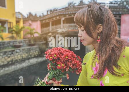 Fuoco selettivo sui fiori rossi, belle donne in Ao dai Vietnam abito tradizionale holidng un ramo di fiori rossi Foto Stock