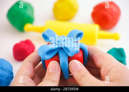 Bambino che tiene il regalo di creta di gioco avvolto con nastro blu. La scatola regalo e il nastro sono fatti di creta di gioco (plastilina). Foto Stock
