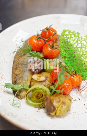 Filetto di walleye fritto con patate, porri, pomodori ciliegini e funghi sul piatto Foto Stock