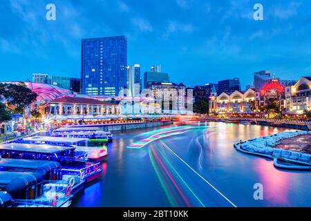 Tramonto vita notturna a Clarke Quay sul fiume Singapore come colorati sentieri luce dalle barche del fiume e bar e ristoranti circostanti illuminare la popula Foto Stock