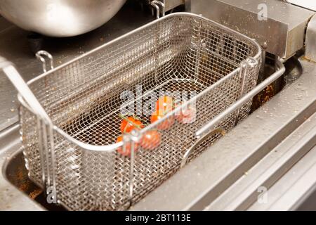 Fornello Friture in cucina ristorante, pomodori ciliegini circa per essere fritti in profondità Foto Stock