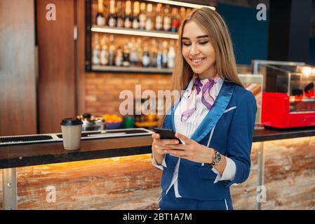 Hostess tramite cellulare in aeroporto cafe. Hostess di aria nella zona attesa, assistente di volo in partenza, area lavoro aviatransportations Foto Stock