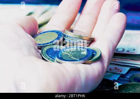 La mano della donna tiene una e due monete Euro, stile di colore freddo Foto Stock
