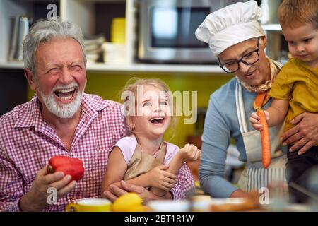 Nonni felici con i nipoti piccoli che fanno colazione in cucina. Foto Stock