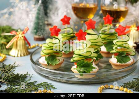 Tartine festive a forma di alberi di Natale in cetrioli e stelle di peperone su sfondo azzurro con due bicchieri di vino, Closeu Foto Stock