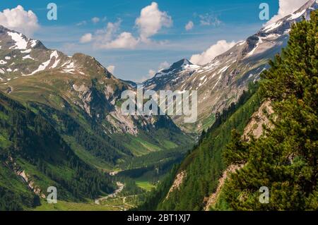 Veduta aerea delle Alpi austriache con la strada sterrata in Valle e le cime di montagna coperte di macchie di neve. Foto Stock