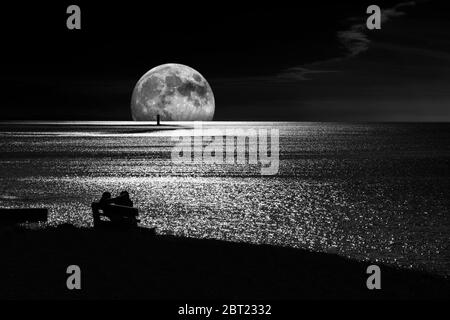 Una giovane coppia guarda una superluna surrealistica che si erge dietro il faro di Blackrock al largo di Rosses Point, County Sligo, Irlanda Foto Stock