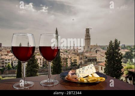 Due bicchieri di vino con assortimento di salumi con vista su Verona. Bicchiere di vino rosso con diversi spuntini - piatto con prosciutto, affettato, formaggio Foto Stock