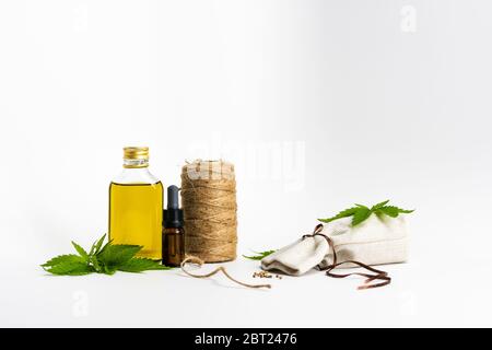 Bottiglie di vetro con olio essenziale CBD, foglia di marijuana medica, semi e filo di canapa su sfondo bianco, primo piano. Concetto di uso della cannabis nel tessuto Foto Stock