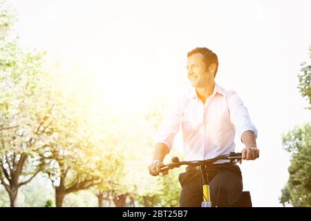 Uomo d'affari in bicicletta durante la soleggiata giornata estiva nel parco Foto Stock
