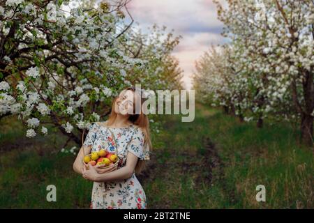 Una ragazza sorridente in un vestito bianco si trova in un bellissimo frutteto di mele Foto Stock