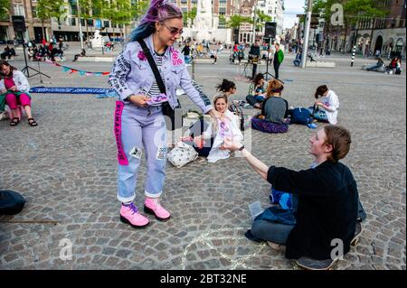 Un attivista XR distribuisce volantini sull'azione.l'estinzione Rebellion Nederland ha organizzato un'azione di moda XR, per mostrare un'alternativa all'industria frenetica della moda. Circa venti attivisti si sono esibiti in piazza Dam, nel centro di Amsterdam, per cucire e riparare i vestiti usati, per sostenere le piccole etichette di moda sostenibili che stanno attraversando un momento difficile, e due volte pensando prima di acquistare nuovi vestiti. Durante l'azione, e secondo le regole di Coronavirus, gli attivisti hanno mantenuto la distanza sociale. Foto Stock