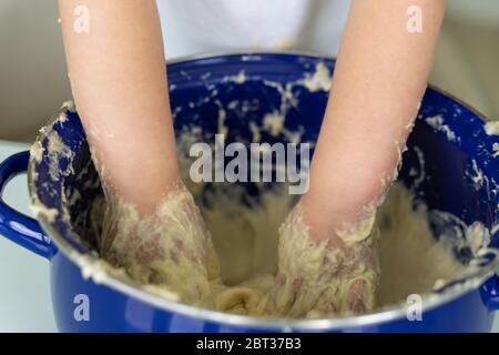 il bambino impasta l'impasto di lievito in una padella blu, le mani si vestiscono. Foto Stock