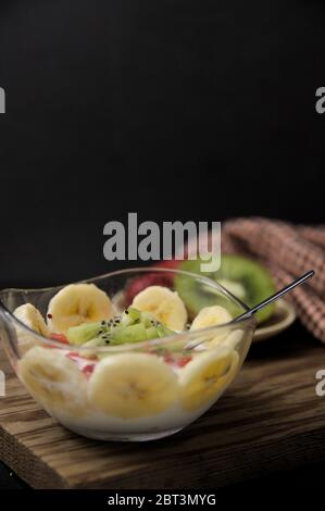 Vista frontale di una ciotola con un mix di yogurt con frutta (banane, kiwi, fragole) con spazio per testi (testo in copia) e sfondo scuro nel f scuro Foto Stock