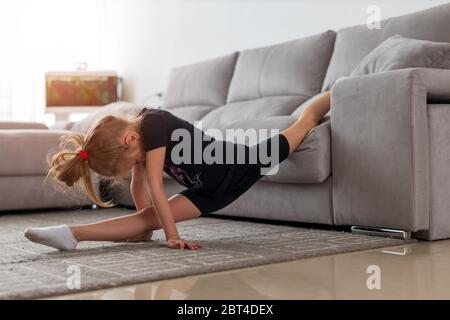 Esercitazioni mattutine. Carino ginnasta pratica che allunga ogni mattina. Ragazza bambino che si allunga sul tappeto. Tempo per lo stretching mattutino. Ragazza capretto capelli biondi Foto Stock