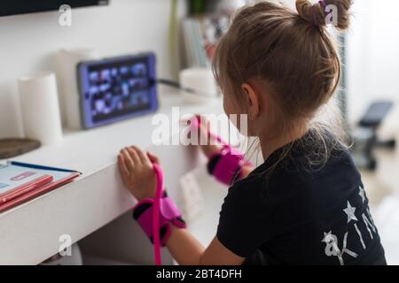 Bella ragazza giovane in sportswear guardando video online su computer portatile e facendo esercizi di fitness a casa. Formazione a distanza con personal trainer, di Foto Stock