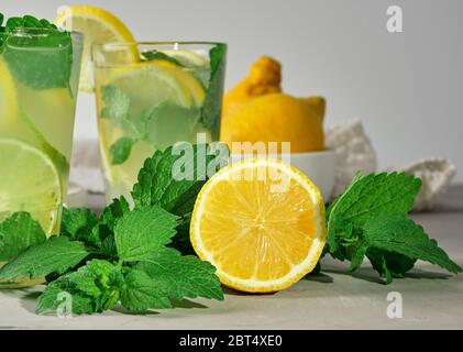 La metà di un limone giallo e verde fresco menta, accanto a due bicchieri con un estate bevanda rinfrescante Foto Stock