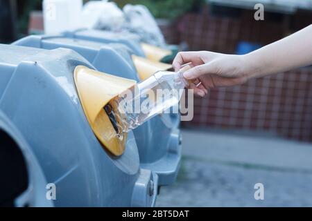 Closeup donna mano gettando bottiglia vuota di plastica in contenitore di riciclaggio. Isolato esterno sfondo. Foto Stock