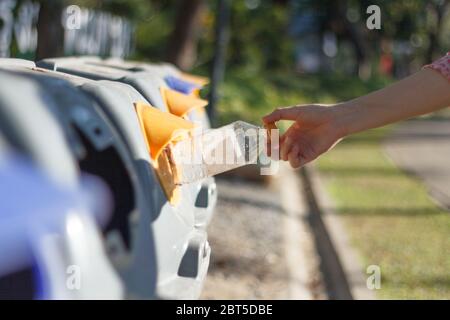 Closeup donna mano gettando bottiglia vuota di plastica in contenitore di riciclaggio. Isolato esterno sfondo. Foto Stock