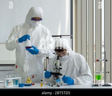 I ricercatori utilizzano i microscopi per esaminare i campioni di sangue delle persone infette. Coronavirus Disease 2019 (COVID-19) processo di analisi in un laboratorio preventin Foto Stock