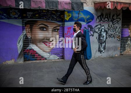 Mexiko Stadt, Messico. 16 maggio 2020. Una mariachia con una guardia della bocca cammina di fronte a un murale di Aida Cuevas, un'icona della musica messicana. La mariachia del Messico è in difficoltà perché le misure anticorona li privano della loro sussistenza. (A dpa 'Serenade Against Donation: Mariachis in Mexico chiedere 'scue') credito: Jair Cabrera Torres//dpa/Alamy Live News Foto Stock