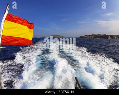 mare blu di ​​ibiza vicino alla costa con tracce delle linee di schiuma lasciate da una barca e la bandiera spagnola a lato dell'isola delle baleari Foto Stock