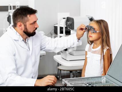 Medico che tiene l'attrezzatura speciale dell'occhio che esamina gli occhi della ragazza nella clinica oftalmologica Foto Stock