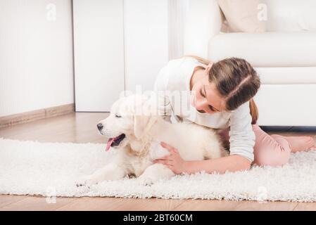 Ragazza sorridente mentendo con carino peluche di Retriever peloso abbracciare sul tappeto Foto Stock