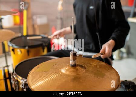 Mano di giovane musicista in felpa nera che tiene il batterista sopra i piatti mentre andando batterlo durante le prove nel suo garage o studio Foto Stock