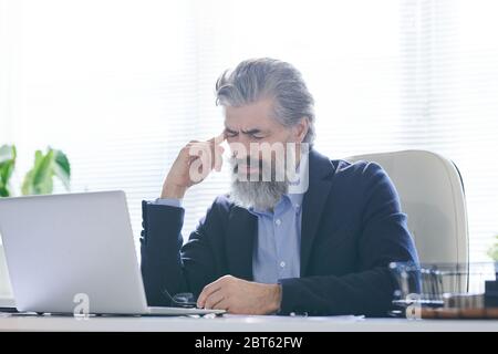 Uomo anziano stanco o pensivo con barba grigia e capelli che toccano il tempio mentre soffre di mal di testa o cercando di ricordare qualcosa Foto Stock